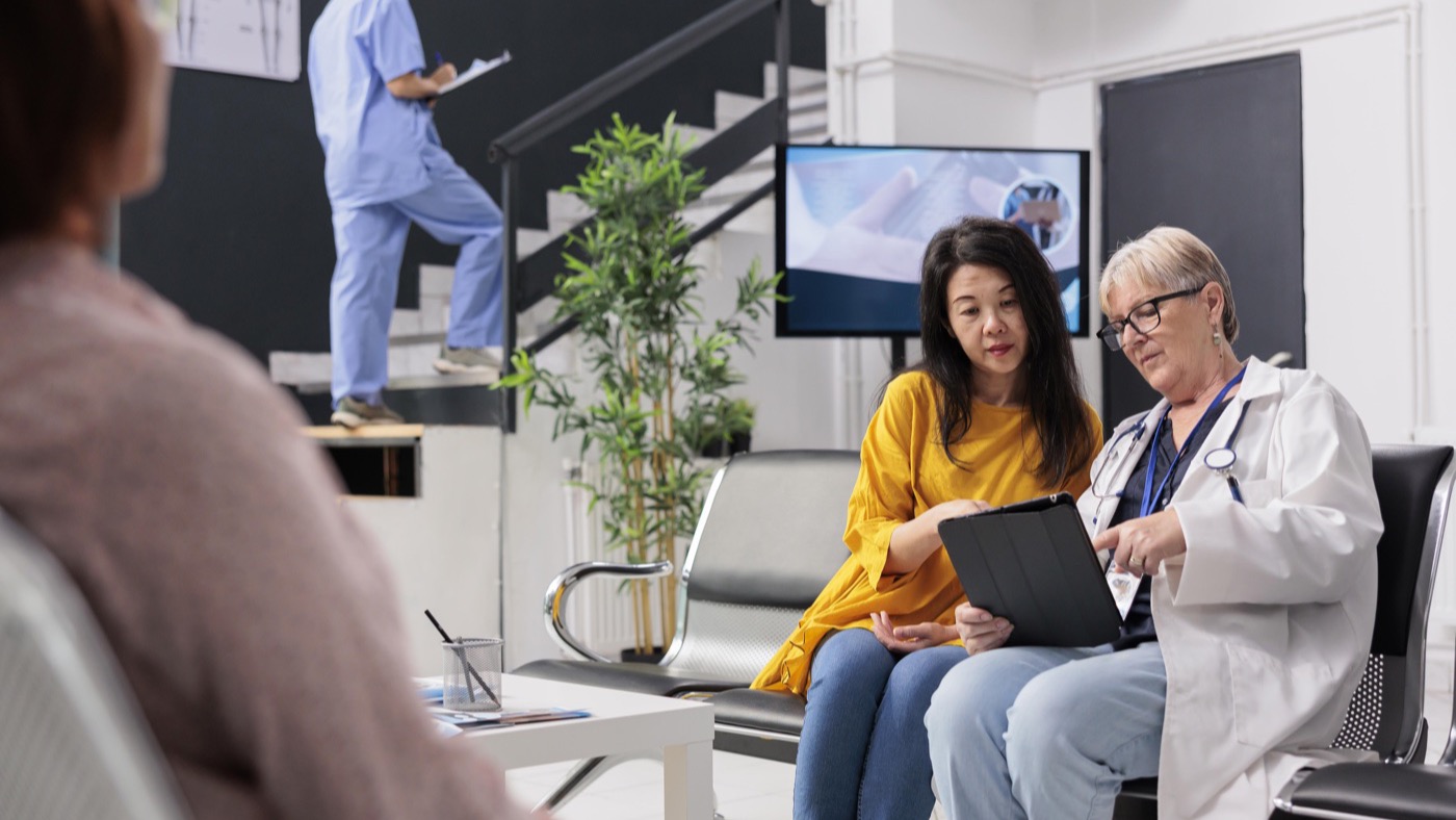 A doctor and a patient looking at a tablet together in a clinic waiting area